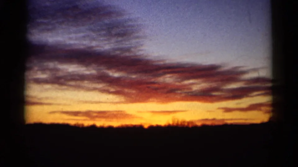 Final 8mm sunset frame showing warm orange light near the horizon and darker cloud bands across the sky.
