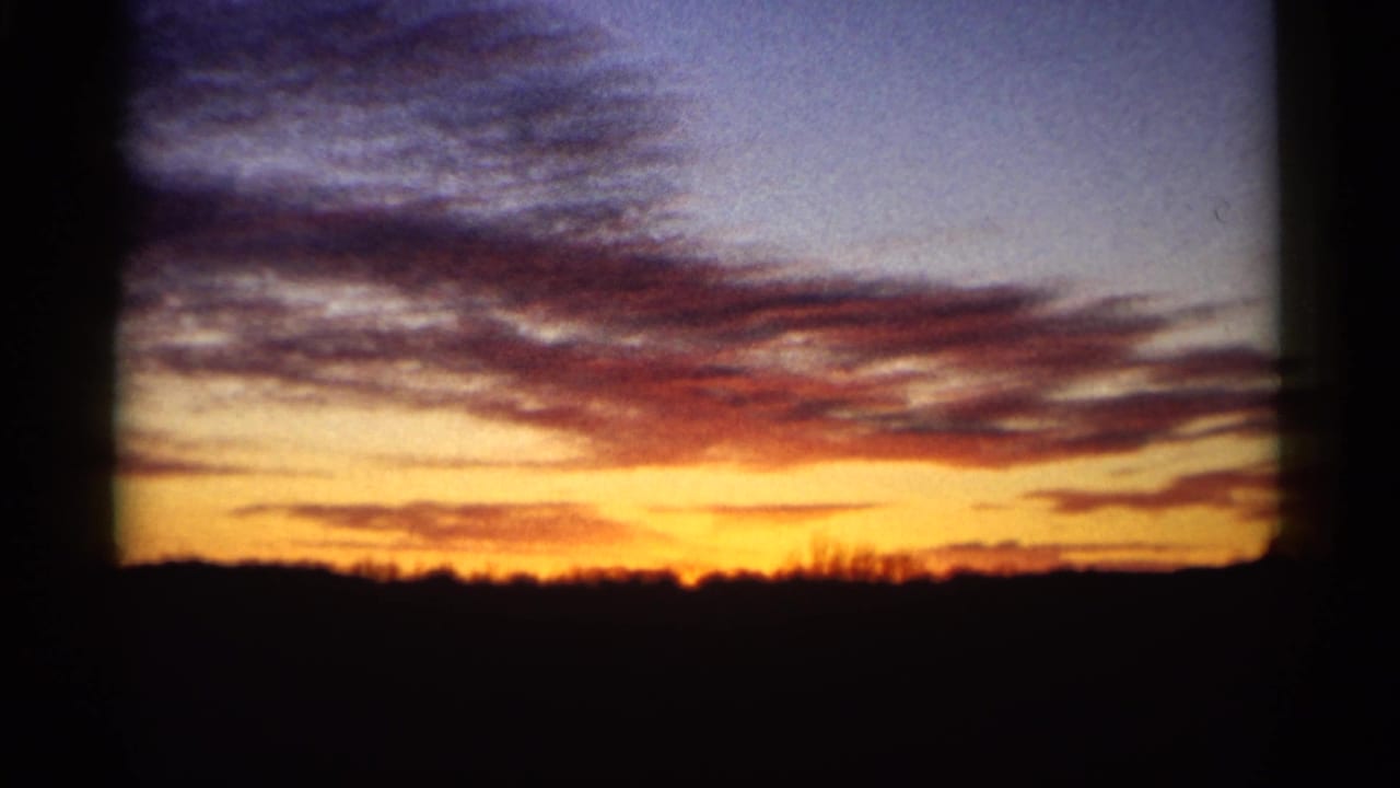 Orange sunset beneath purple clouds over a dark rural horizon.