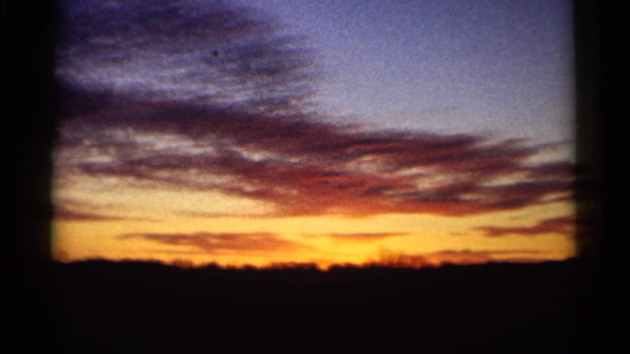 1961 Minnesota home-movie frame with a bright orange-yellow sunset band, cloud layers, and a silhouetted horizon.