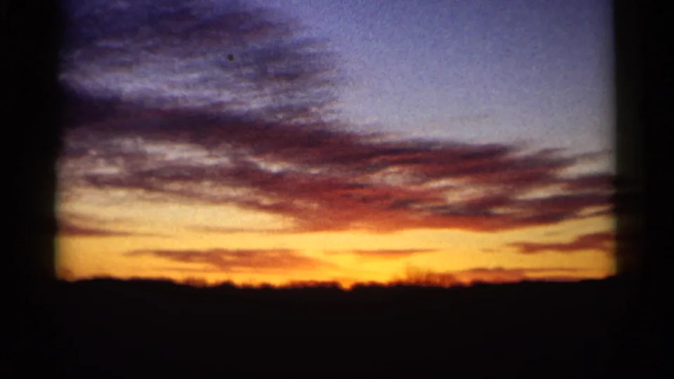 1961 Minnesota home-movie frame with a bright orange-yellow sunset band, cloud layers, and a silhouetted horizon.
