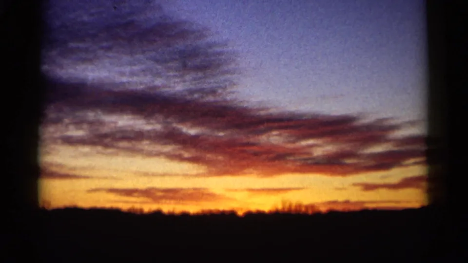 1961 Minnesota 8mm still showing soft sunset color, purple cloud cover, and a low silhouetted rural landscape.