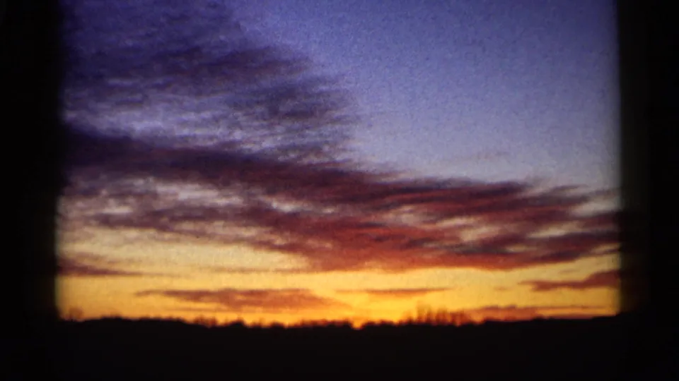 1961 Minnesota home-movie frame of red-purple evening clouds and orange light above a dark rural horizon.
