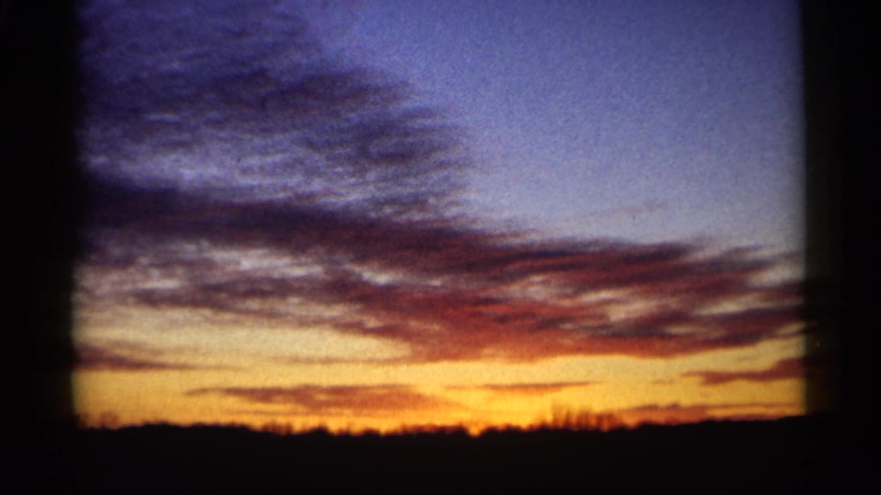1961 Minnesota 8mm frame showing an orange sunset band, blue-purple cloud cover, and a dark rural treeline silhouette.