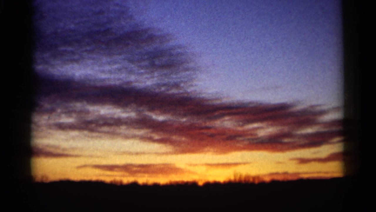 1961 Minnesota 8mm view of a rural sunset with orange light near the horizon and layered blue clouds above a silhouetted treeline.