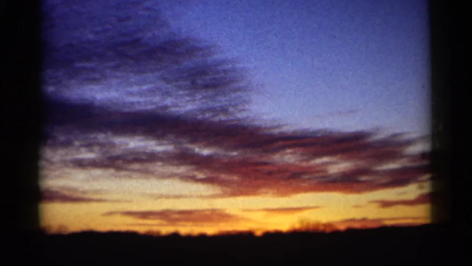 1961 Minnesota 8mm home-movie frame showing a blue and orange sunset sky over a dark low horizon with streaked clouds and visible film borders.