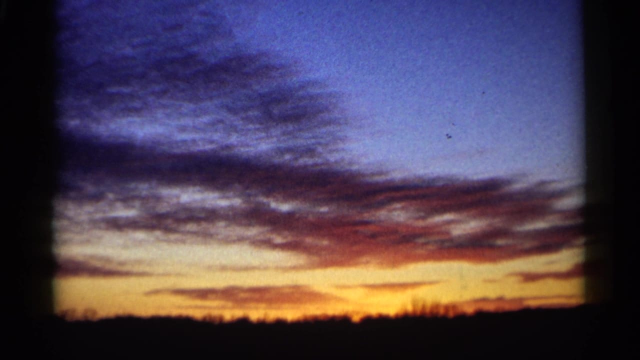 Cloud-streaked sunset with a dark horizon and warm orange light near the bottom of the frame.