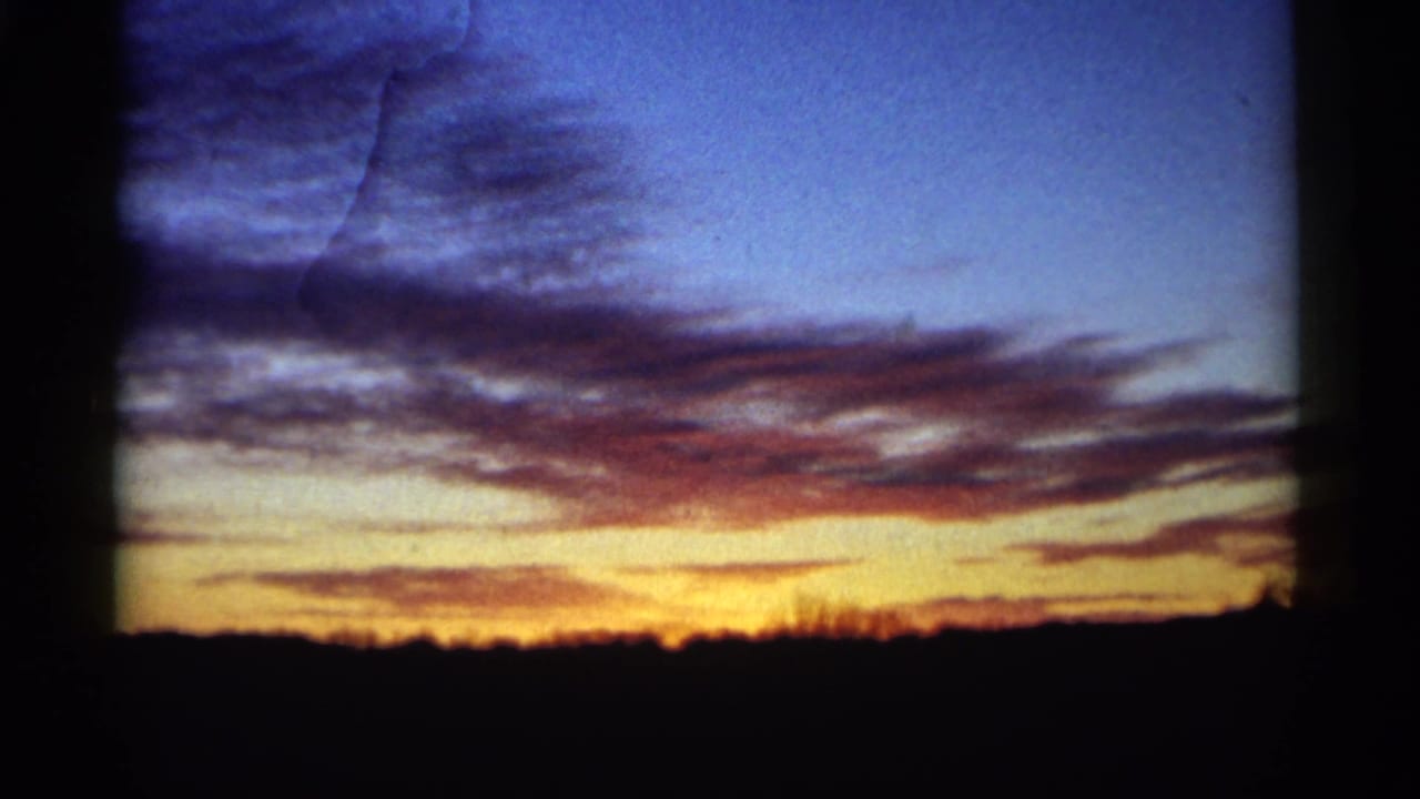 Orange sunset beneath blue and purple clouds over a dark flat horizon.