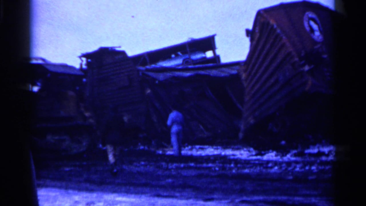Overturned train wreckage in a snowy field with a person standing near the debris.
