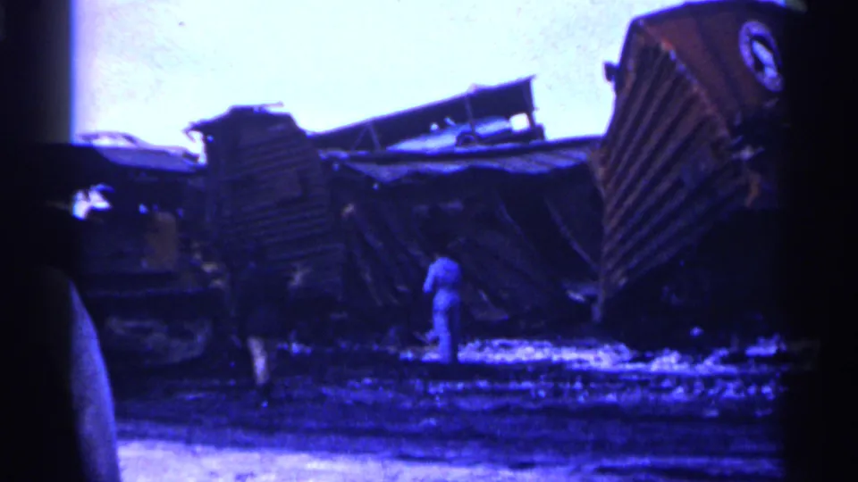 1961 Minnesota 8mm frame showing collapsed rail cars and two adult bystanders surveying the winter train wreckage.