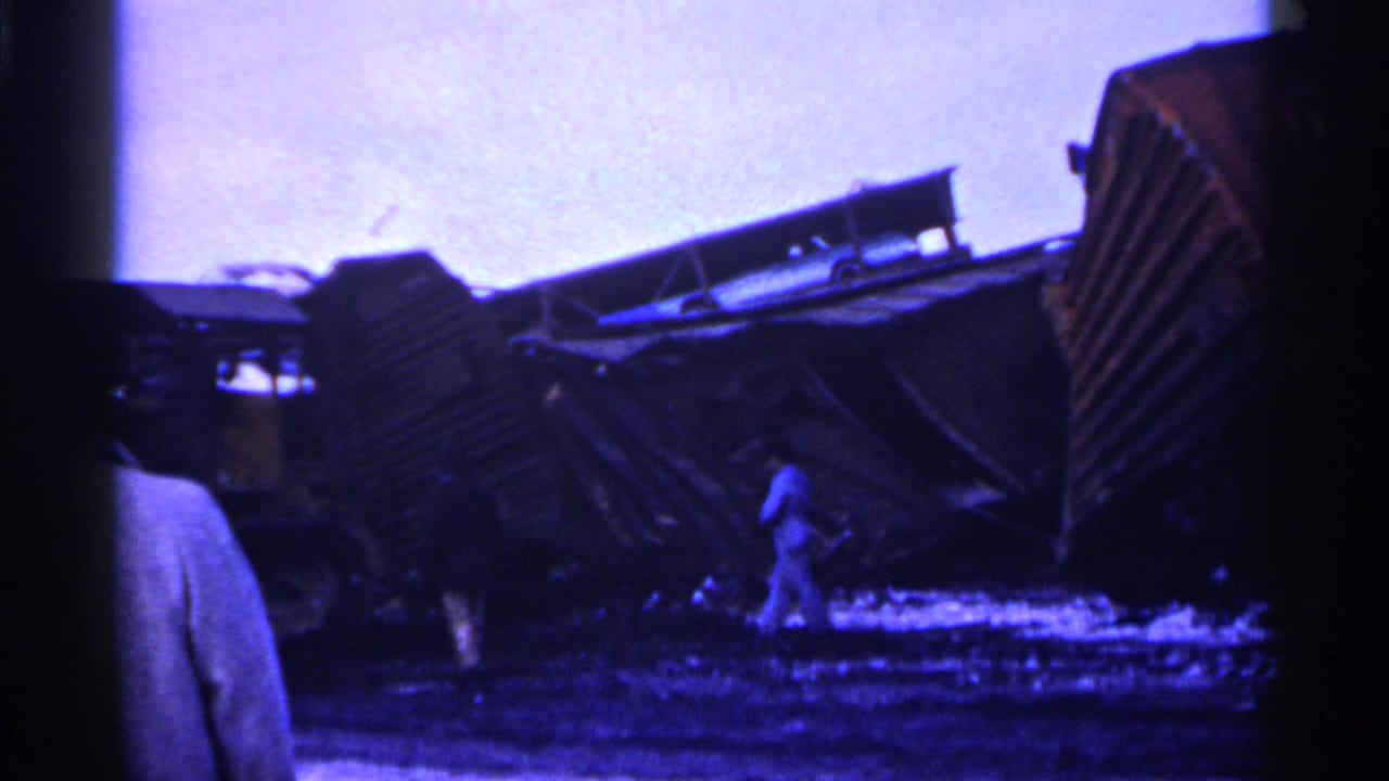 Overturned freight cars and debris with bystanders near the wreckage.