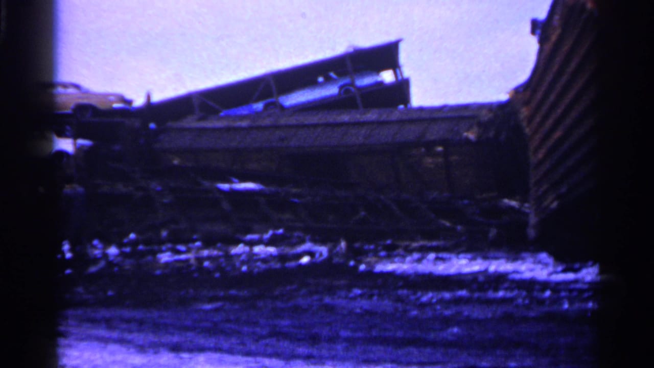 Damaged rail cars with an automobile visible above the wreckage.
