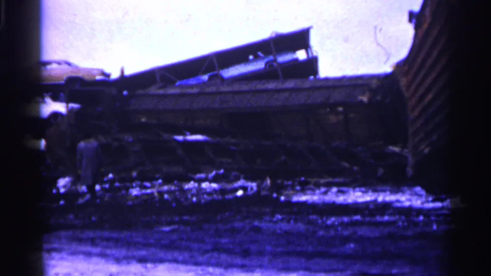 Blue-cast 8mm view of the Minnesota derailment site with damaged cars, debris, and a distant person near the wreckage.