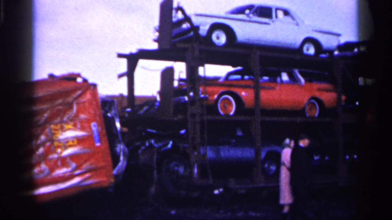 Older cars stacked on a transport vehicle beside a snowy accident scene.