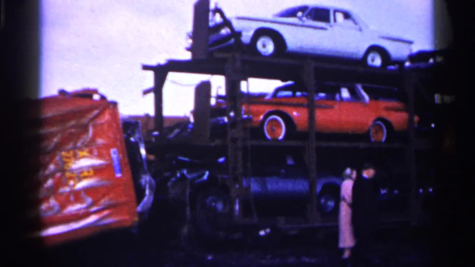 Minnesota 1961 home-movie frame showing older automobiles on a carrier near a snowy rail accident area, with dark film edges.