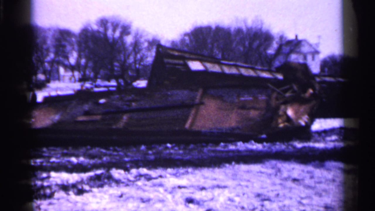 Overturned rail car lying beside snowy ground and leafless trees.
