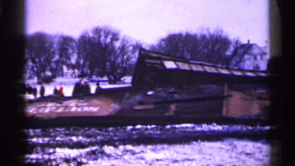 Minnesota 1961 home-movie view of an overturned rail car in snow, with a small group of onlookers near leafless trees.
