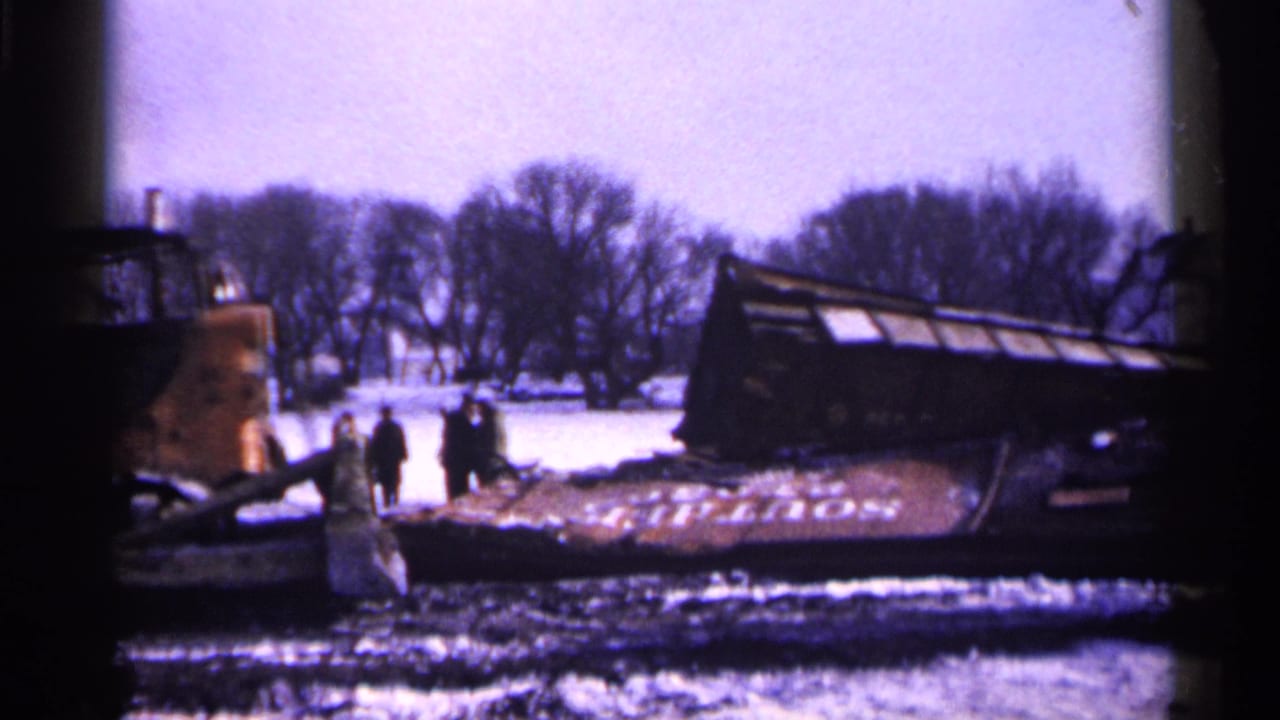 Overturned truck in a snowy area with people nearby and a yellow bulldozer at left.