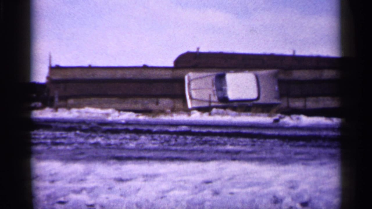 White car angled near a bridge or roadside barrier on snowy ground.