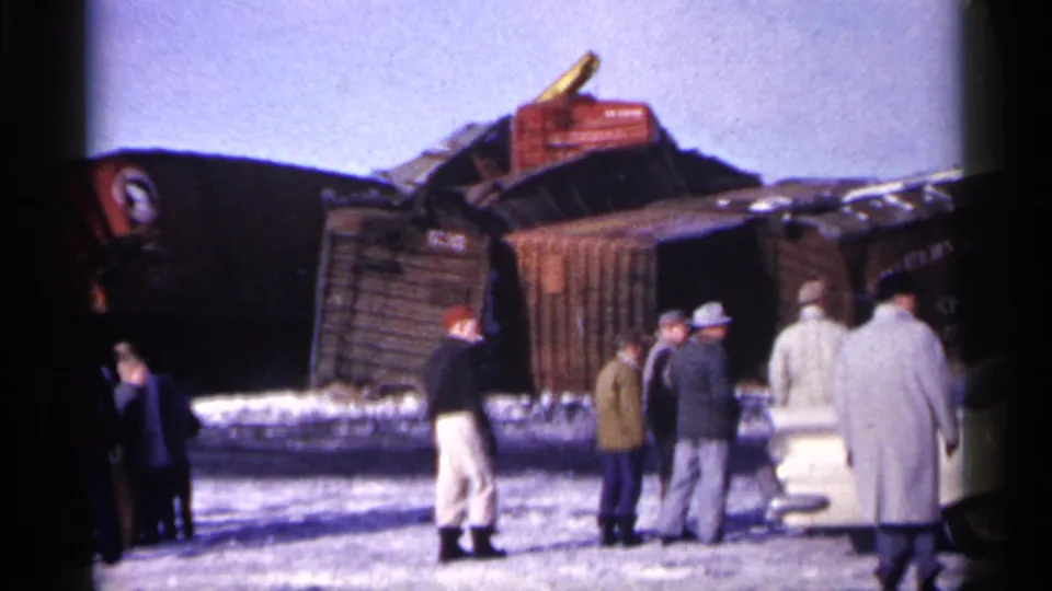 1961 Minnesota 8mm frame with civilians near a parked car observing damaged Great Northern freight cars.