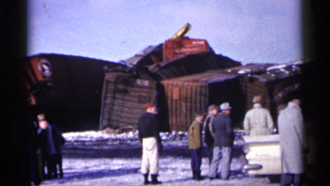 Men stand in snow near overturned freight cars after a train wreck.
