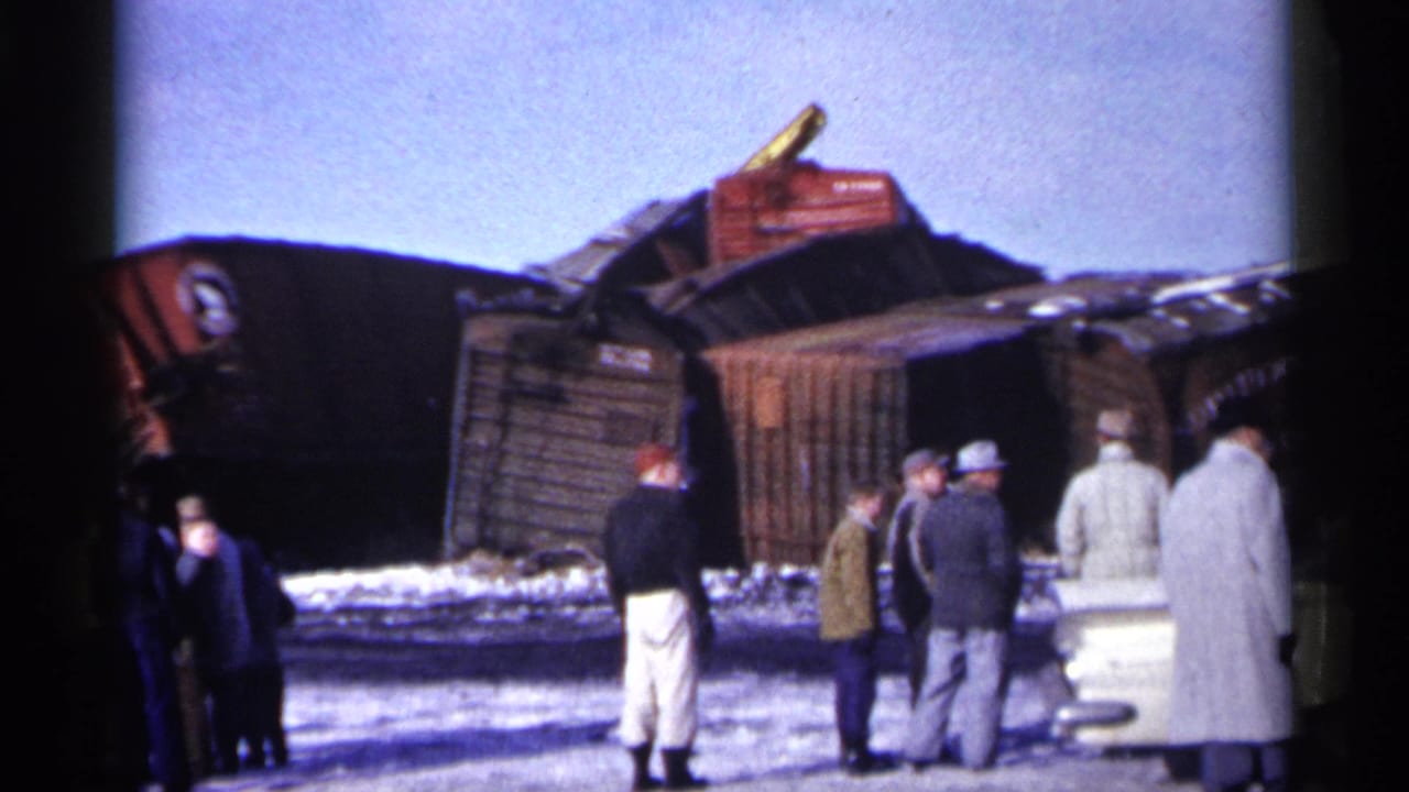 Men in winter coats and hats stand near overturned wooden freight cars in snowy 1961 Minnesota home-movie footage.