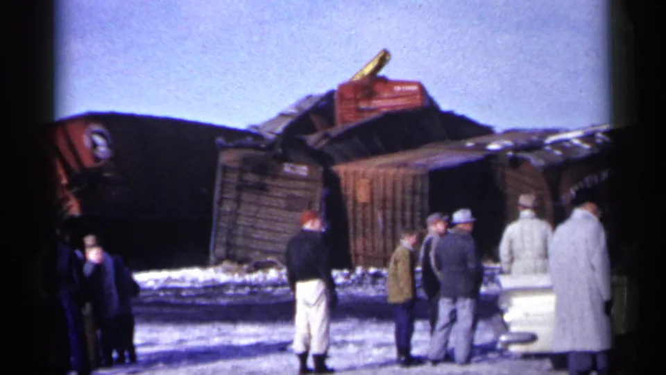 Men in winter coats and hats stand near overturned wooden freight cars in snowy 1961 Minnesota home-movie footage.