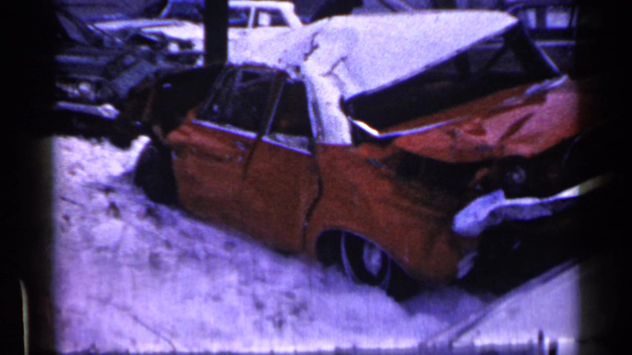 1961 Minnesota home-movie frame showing a wrecked red car with a crushed roof beside snow-covered ground.