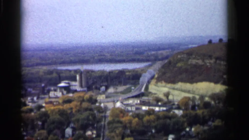 1961 Minnesota 8mm frame showing a distant small town, wide river, bridge, and hillside from an elevated viewpoint.