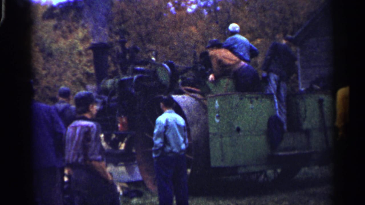 Men in caps and shirts inspect a large green farm machine in a 1961 Minnesota home-movie frame.
