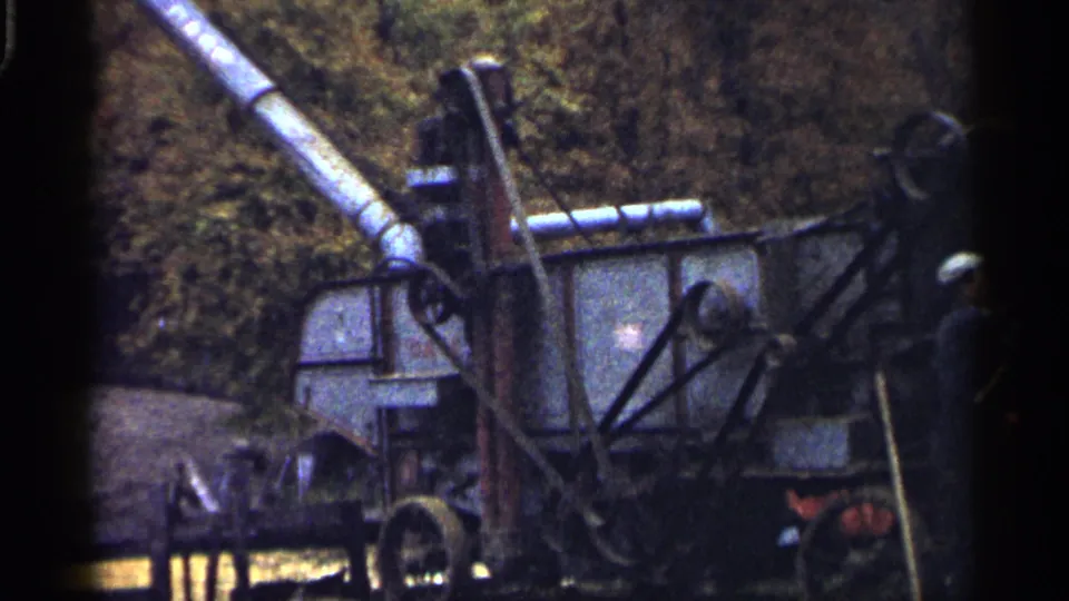 1961 Minnesota frame showing a hay-harvesting machine in close view, with one worker partly visible beside it.