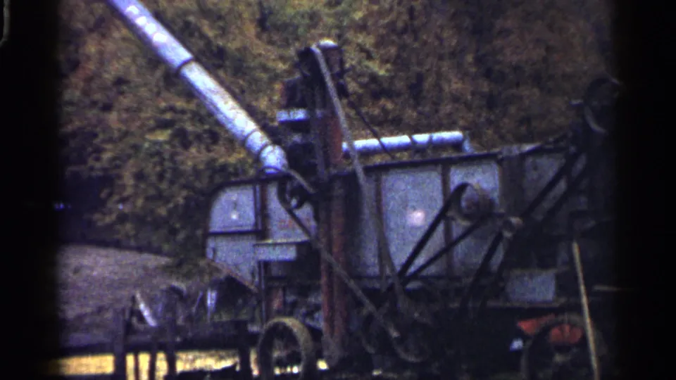 1961 Minnesota 8mm frame showing a weathered farm machine with an extended chute near autumn trees.