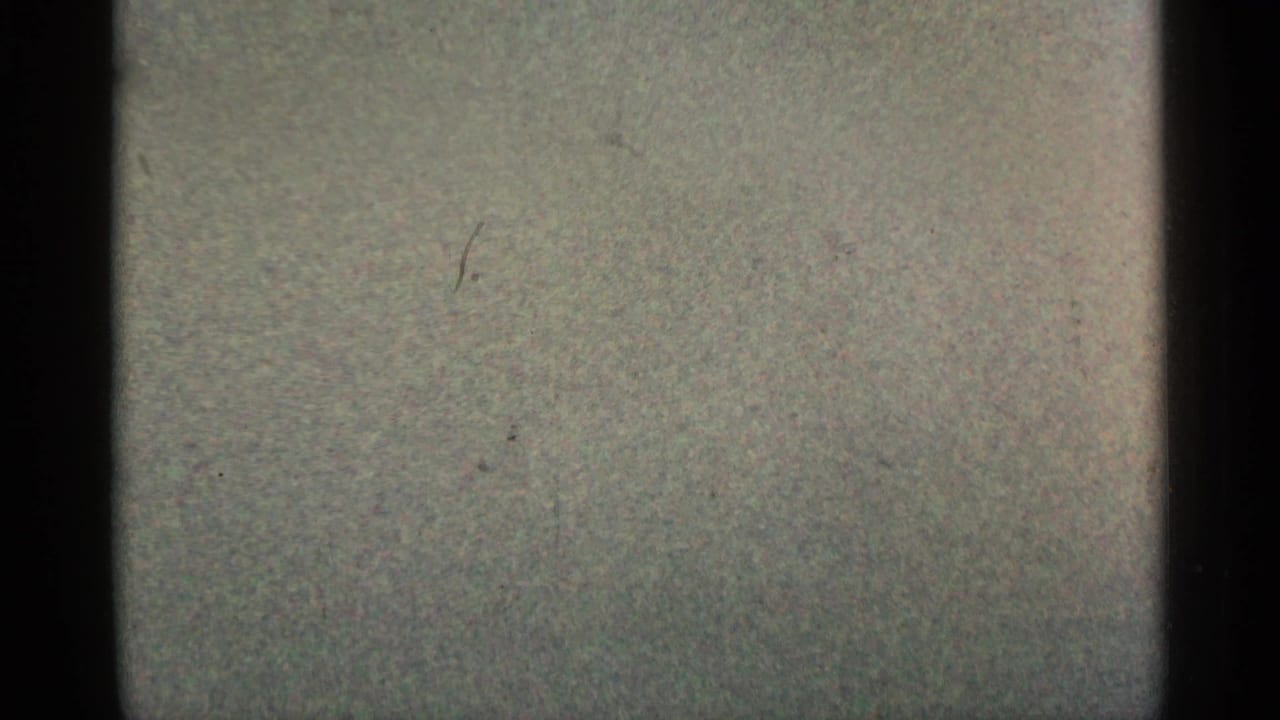 Grainy 8mm frame from the 1961 Minnesota clip showing a pale blank leader-like section with dust marks and dark vertical edge shadow.