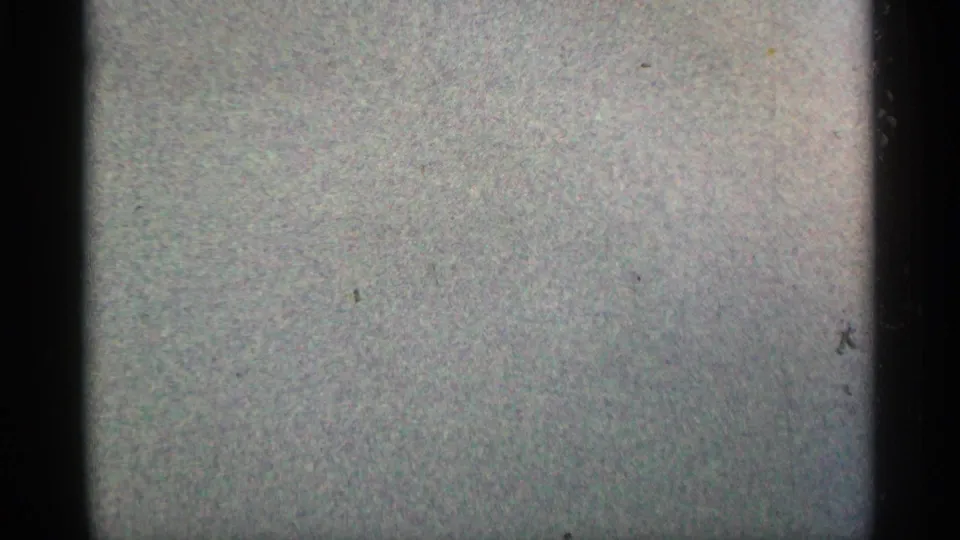 Final 8mm frame shows a pale blank leader-like exposure with visible grain, dark border shadows, and scattered dust specks.