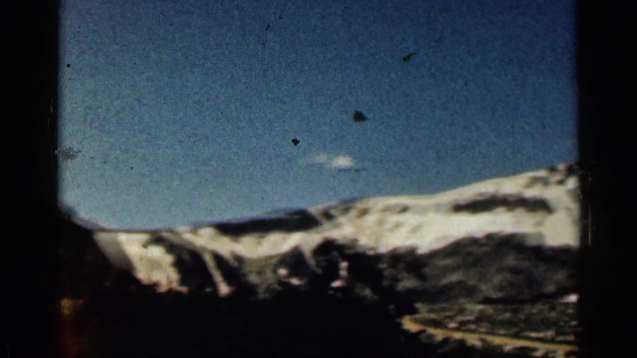 1963 Colorado 8mm frame showing a distant snow-dusted mountain ridge beneath blue sky with dark framing at the edges.