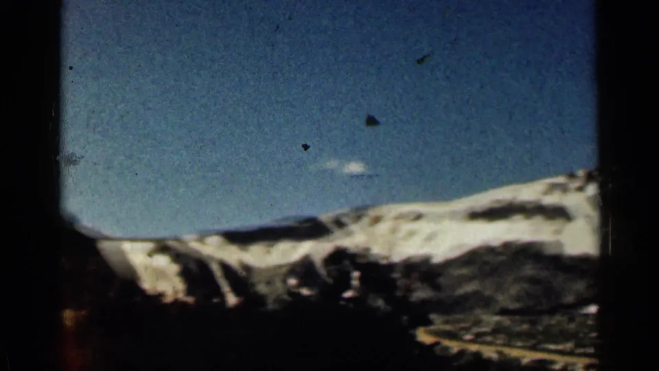 1963 Colorado 8mm frame showing a distant snow-dusted mountain ridge beneath blue sky with dark framing at the edges.