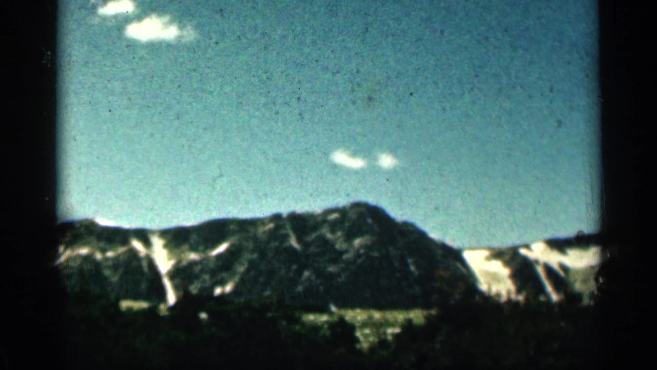 Colorado mountain peak with snow patches and scattered clouds, captured in soft 8mm color from a roadside or vehicle viewpoint.