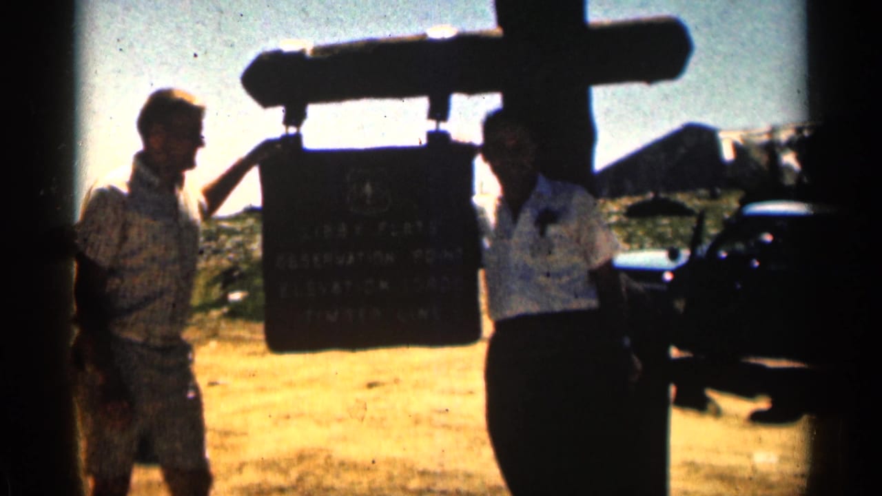 In 1963 Colorado home-movie footage, two adult men stand beside the Libby Flats Observation Point sign with a car in the background.