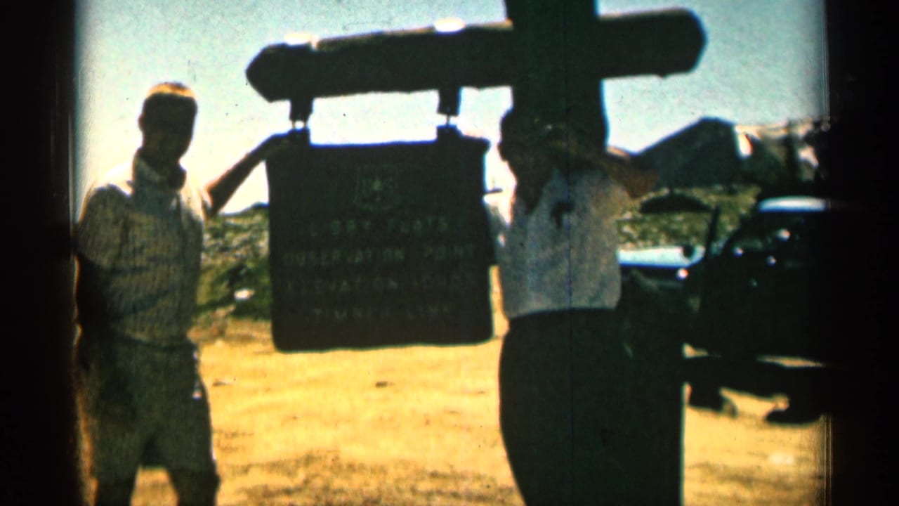 Two men in casual 1960s clothing stand at the Libby Flats Observation Point sign, with a dark car and open landscape behind them.
