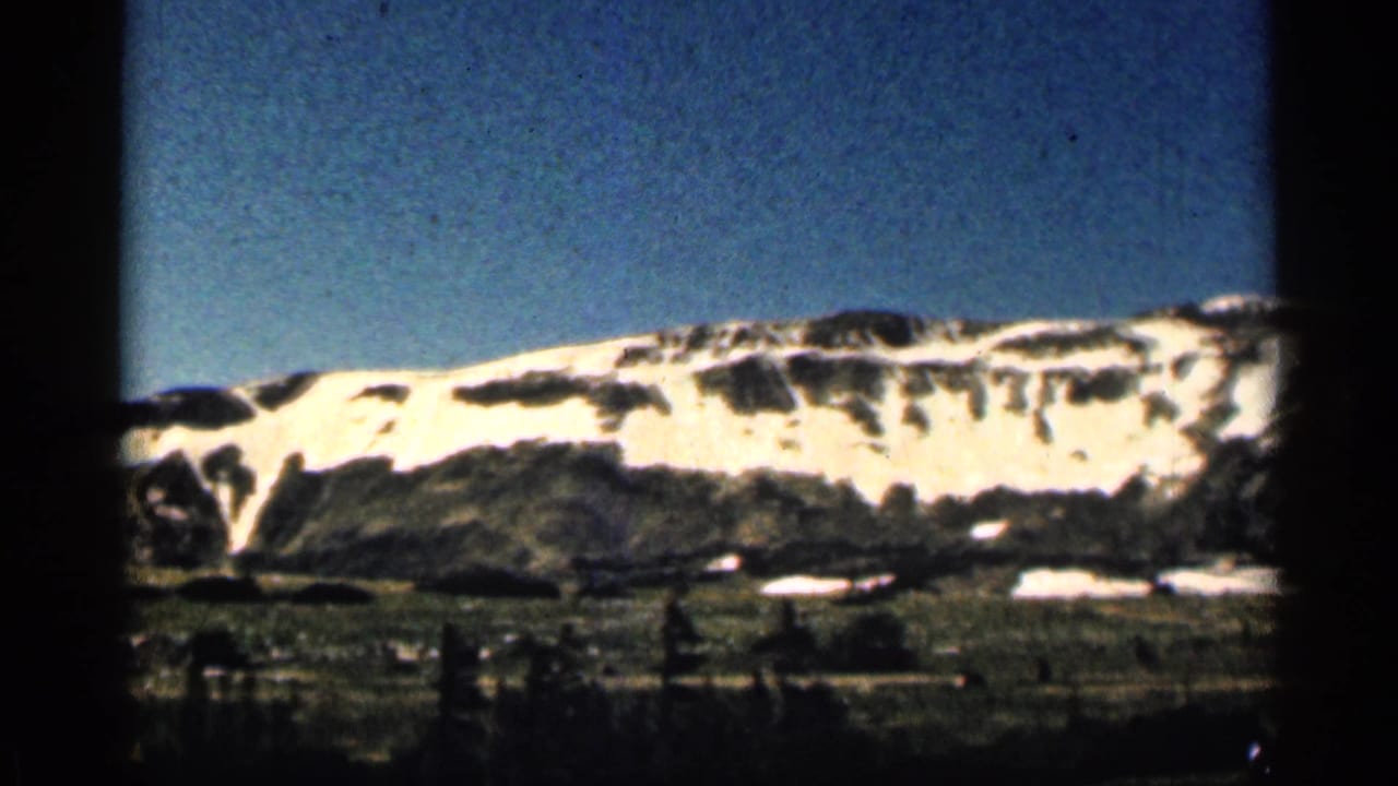 Wide mountain slope with snow patches, blue sky, valley floor, and film gate border.