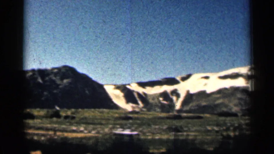 1963 Colorado 8mm frame with a dark rocky slope at left and snowfields crossing the mountain ridge beyond.