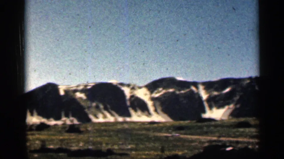 1963 Colorado 8mm closing frame of snow-banded mountain slopes above low valley terrain and pale blue sky.