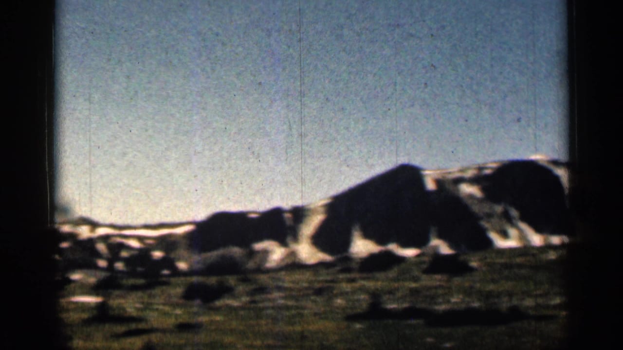 1963 Colorado 8mm frame showing a snow-dusted mountain ridge, dark foreground slope, pale sky, and visible film borders.