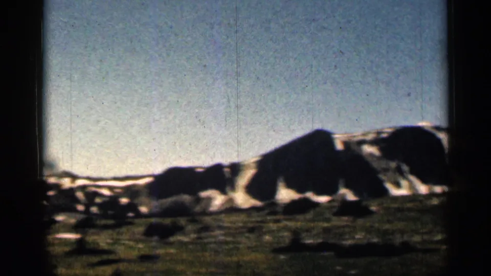 1963 Colorado 8mm frame showing a snow-dusted mountain ridge, dark foreground slope, pale sky, and visible film borders.