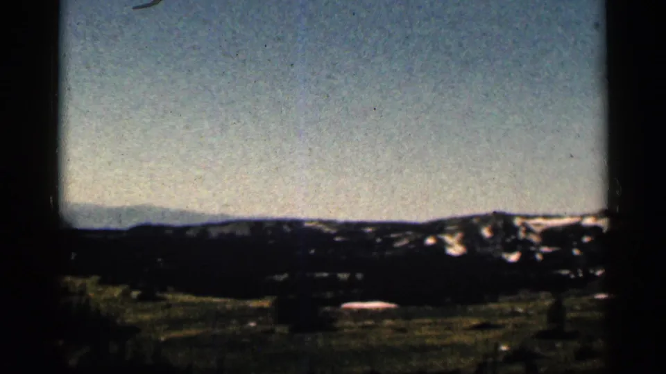 1963 Colorado 8mm view of a distant dark mountain ridgeline with scattered snow patches and a pale open sky.