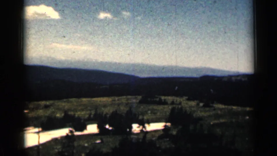 1963 Colorado 8mm frame looking across open terrain toward layered hills, small clouds, and bright lingering snow patches.