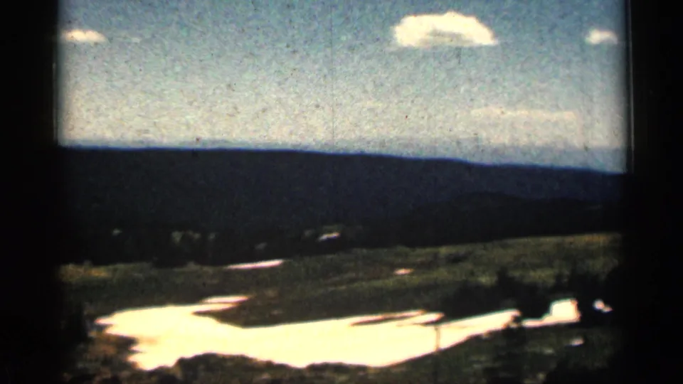 1963 Colorado 8mm landscape showing rolling high-country terrain, bright snowfield patches, distant ridge, and scattered clouds.