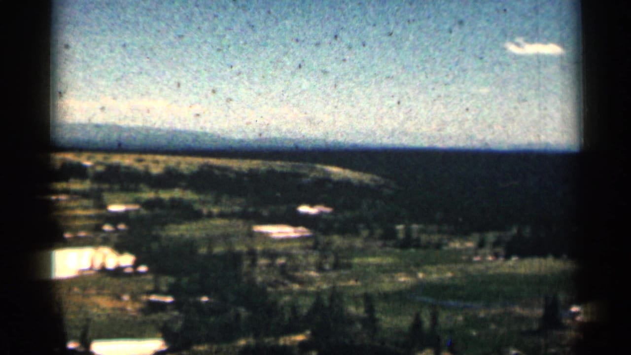 Wide view of open fields, bright snow patches, trees, distant ridge, and blue sky.