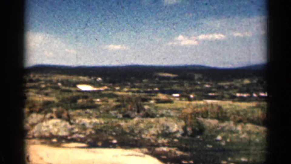 Grainy 1963 Colorado home-movie frame of rocky foreground, grassy open land, and low hills on the horizon.