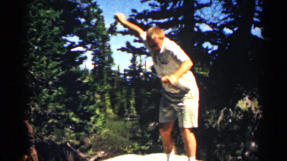 1963 Colorado home-movie frame showing a man moving down a pale rock in a wooded mountain area.
