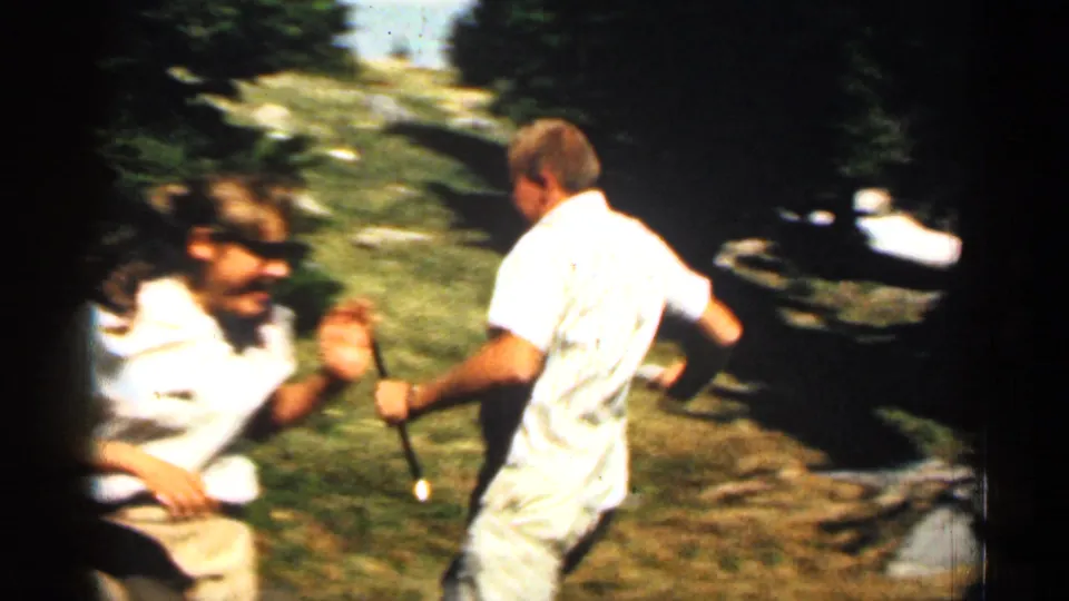 1963 Colorado frame showing two adults sharing a playful moment near rocks in a forested area.